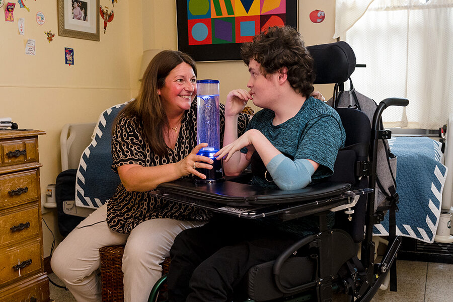 A McGuire Memorial team member is sitting in a resident's room with the resident who is in a wheelchair.