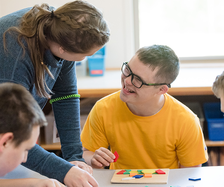 Student in a yellow shirt working on a puzzle. He is smiling up at his instructor.