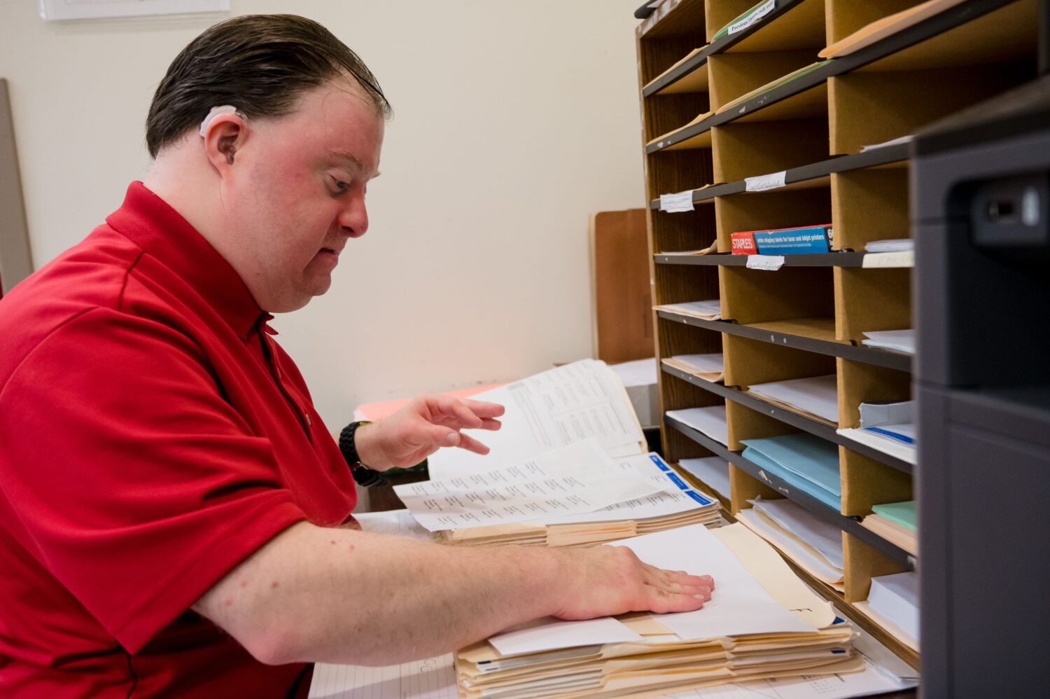 A gentleman in an office setting working on filing and organizing papers and file folders.