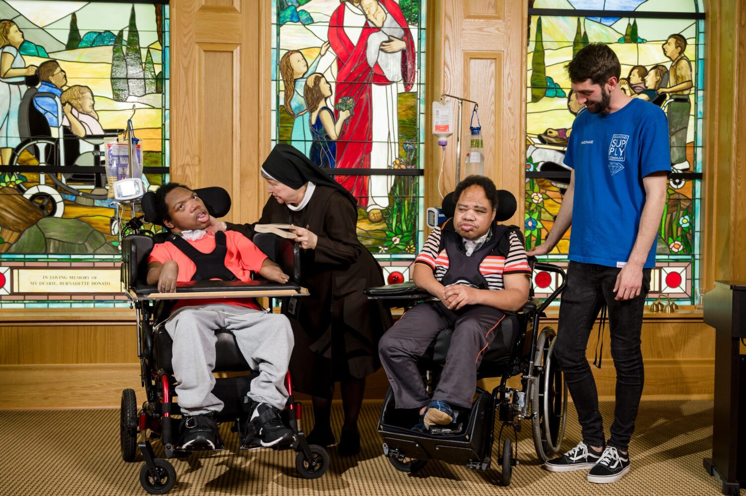 Two residents in wheelchairs are in the McGuire Memorial chapel. With them are a nun and a McGuire Memorial team member.