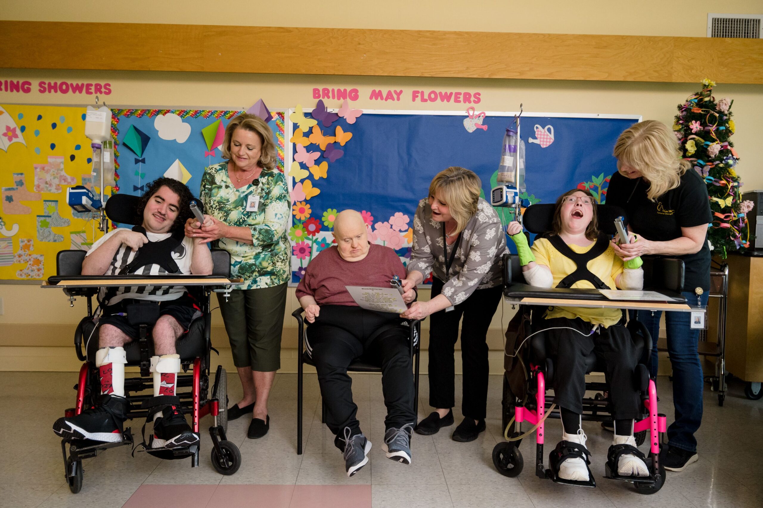 Three McGuire Memorial residents along with three McGuire Memorial team members. Each team member is helping the residents with an activity. In the room is a decorated Christmas tree as well as colorful bulletin boards. 