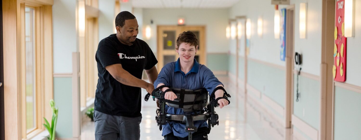 A McGuire Memorial team member is helping a resident walk down the hall with the help of a device.