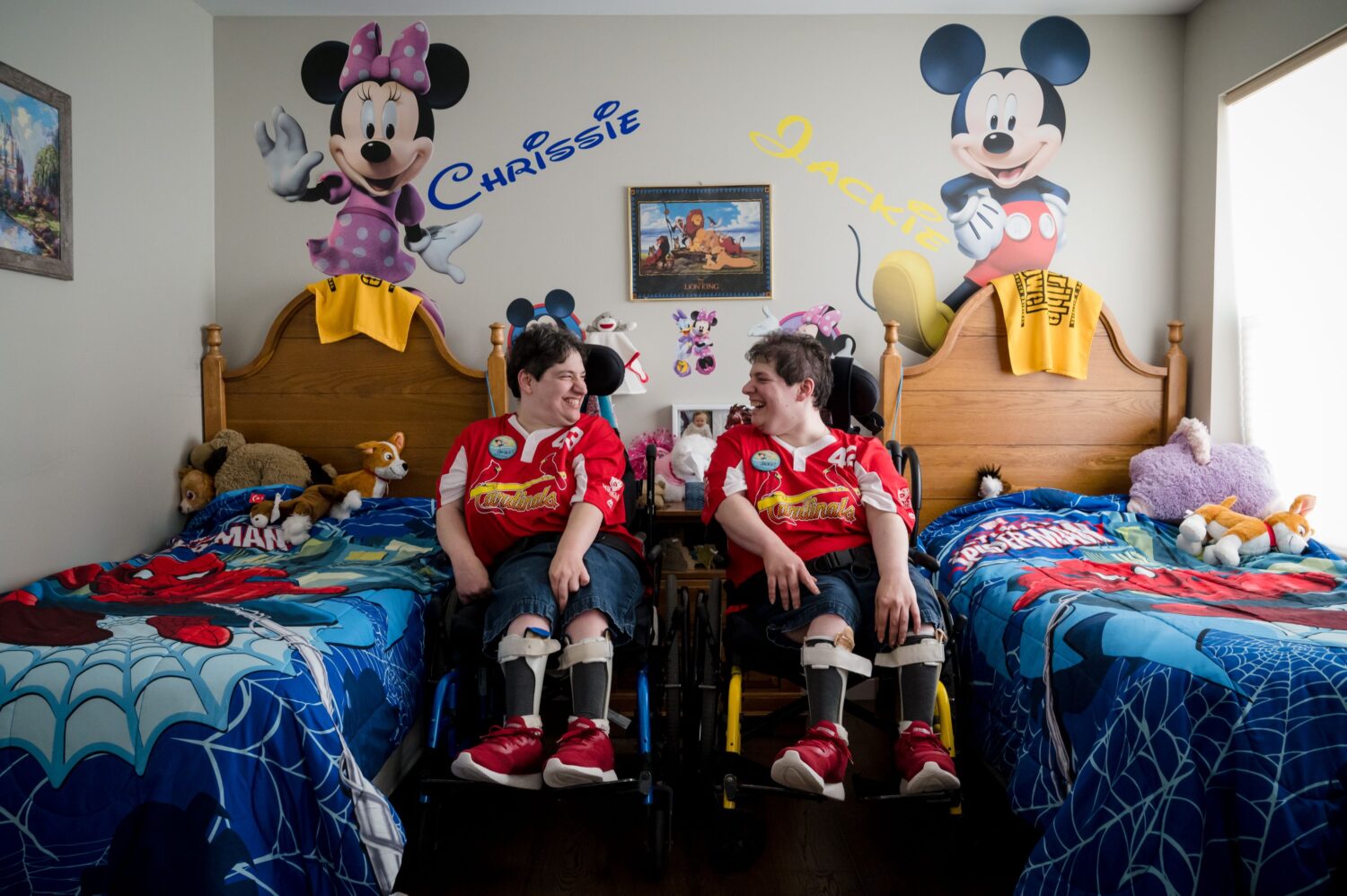 Two residents are in their room at their Community Home. The residents are both in wheelchairs sitting next to their beds. They are smiling at each other.