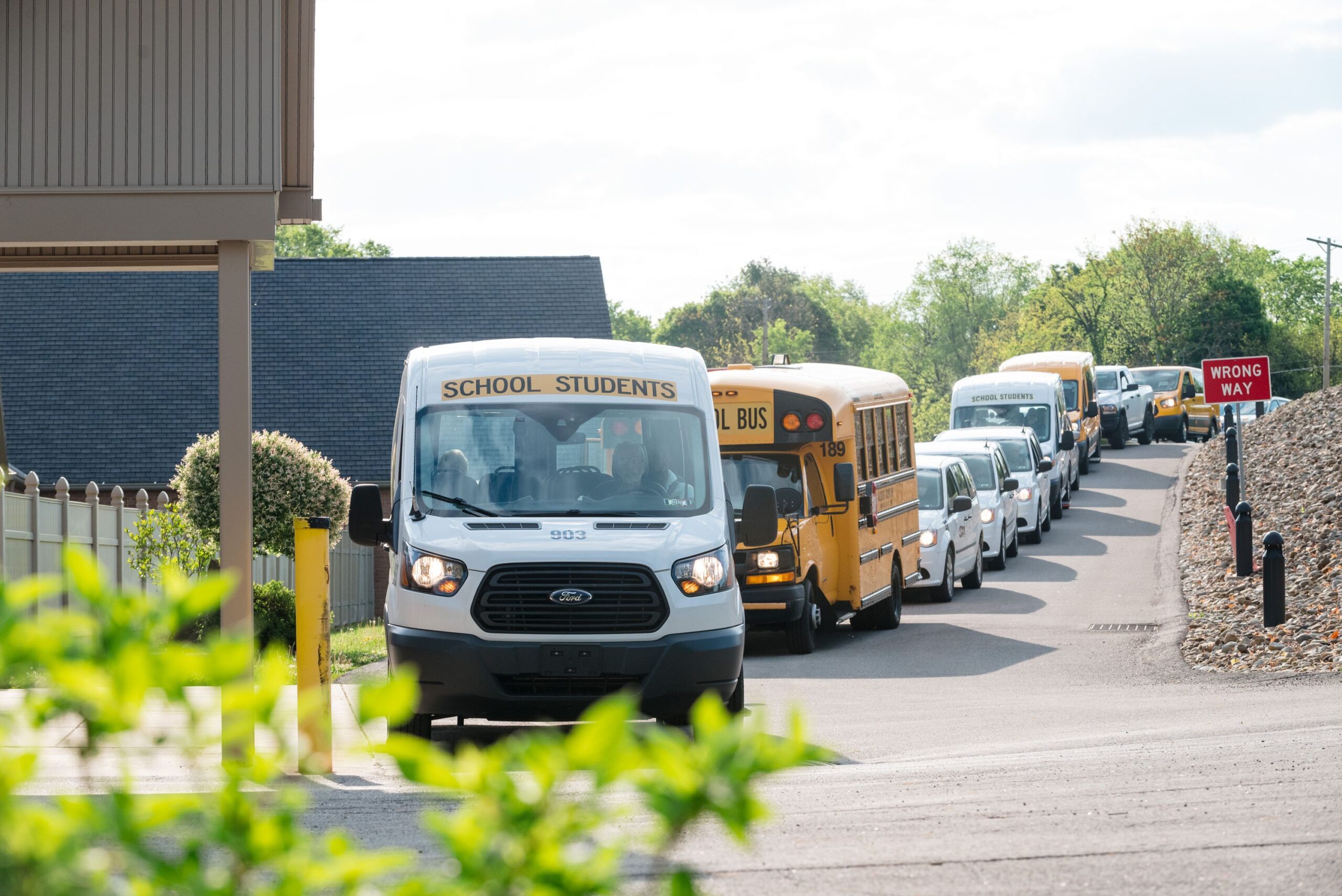 A line of wheelchair accessible vans and school buses are lined up to drop students off at the school. 