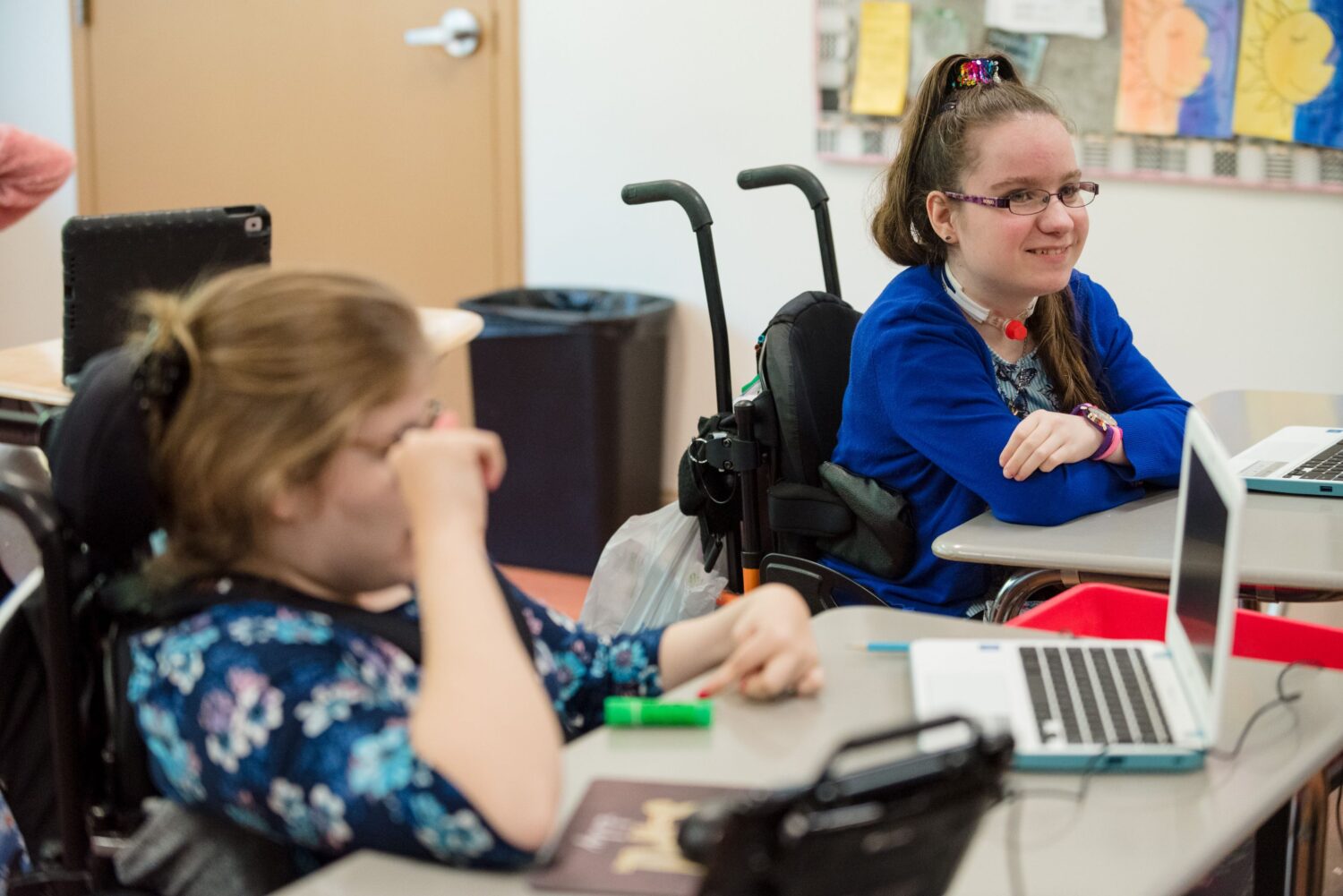 Two female students in wheelchairs sitting at their desks. 