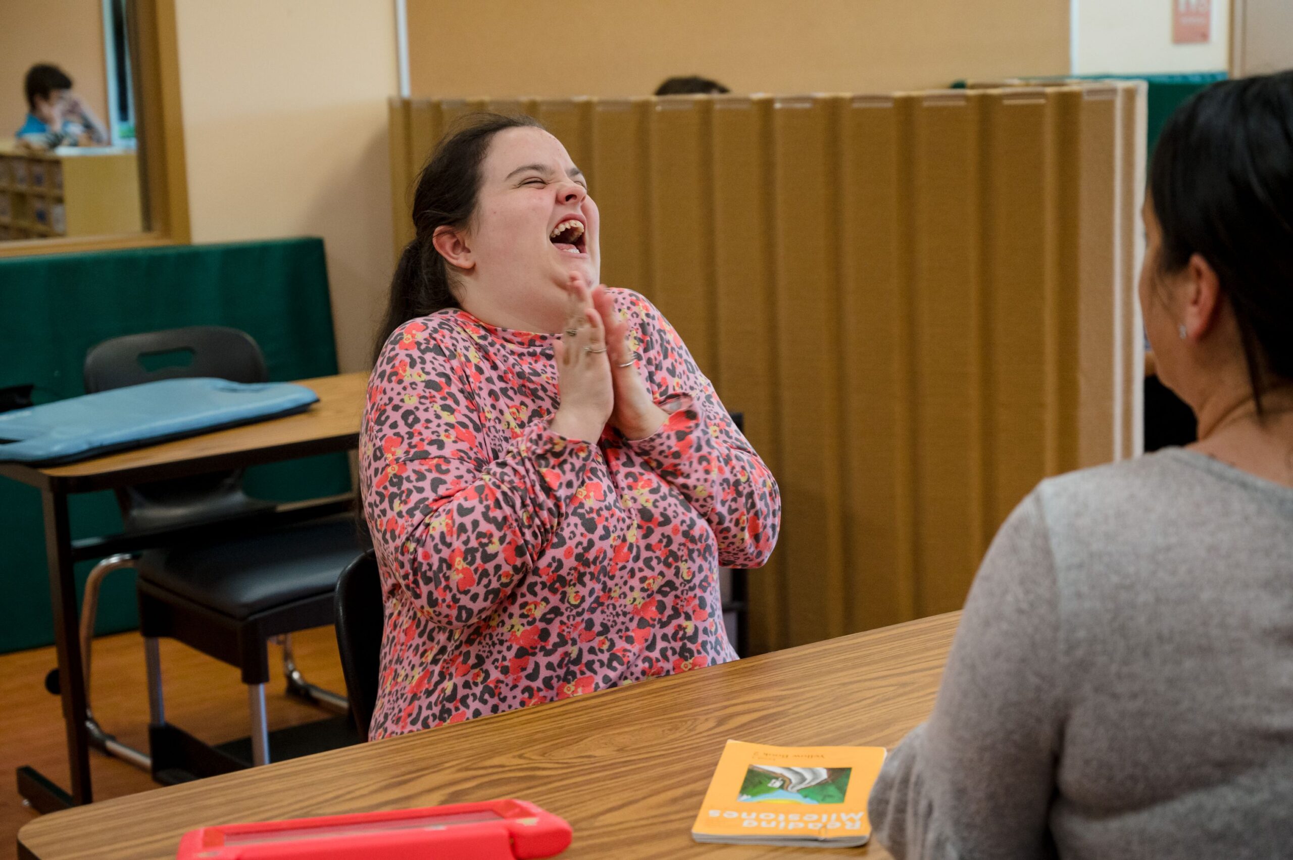 Girl sitting in a classroom smiling and clapping her hands