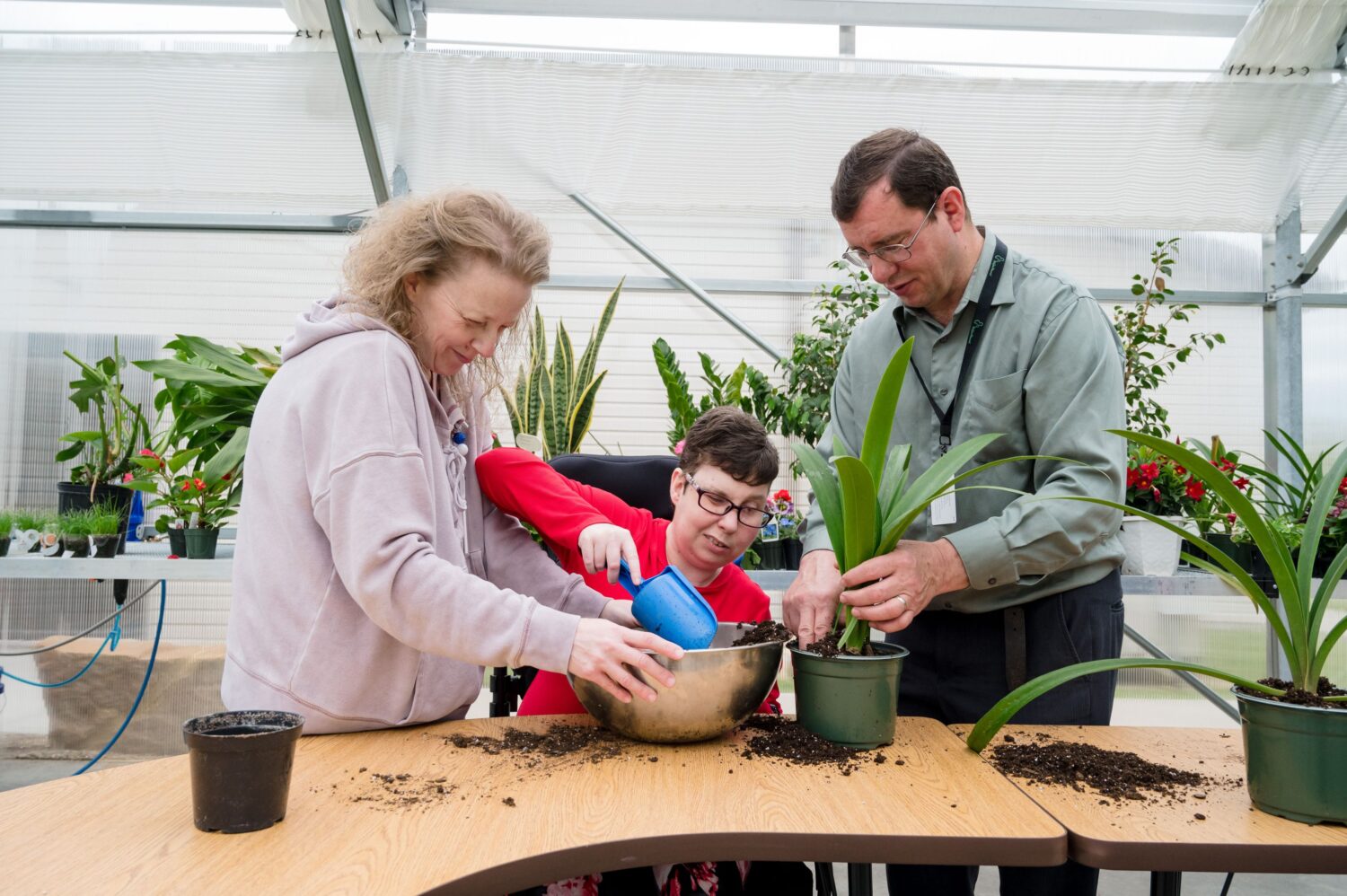 Two McGuire Memorial program instructors helping a LEAP participant pot a plant in the McGuire Memorial greenhouse. 