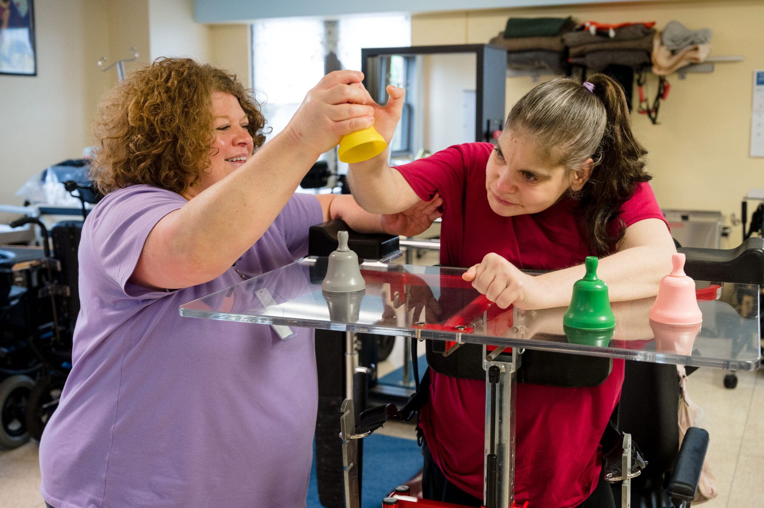 A McGuire Memorial program instructor helping a LEAP participant ring a yellow hand bell. 