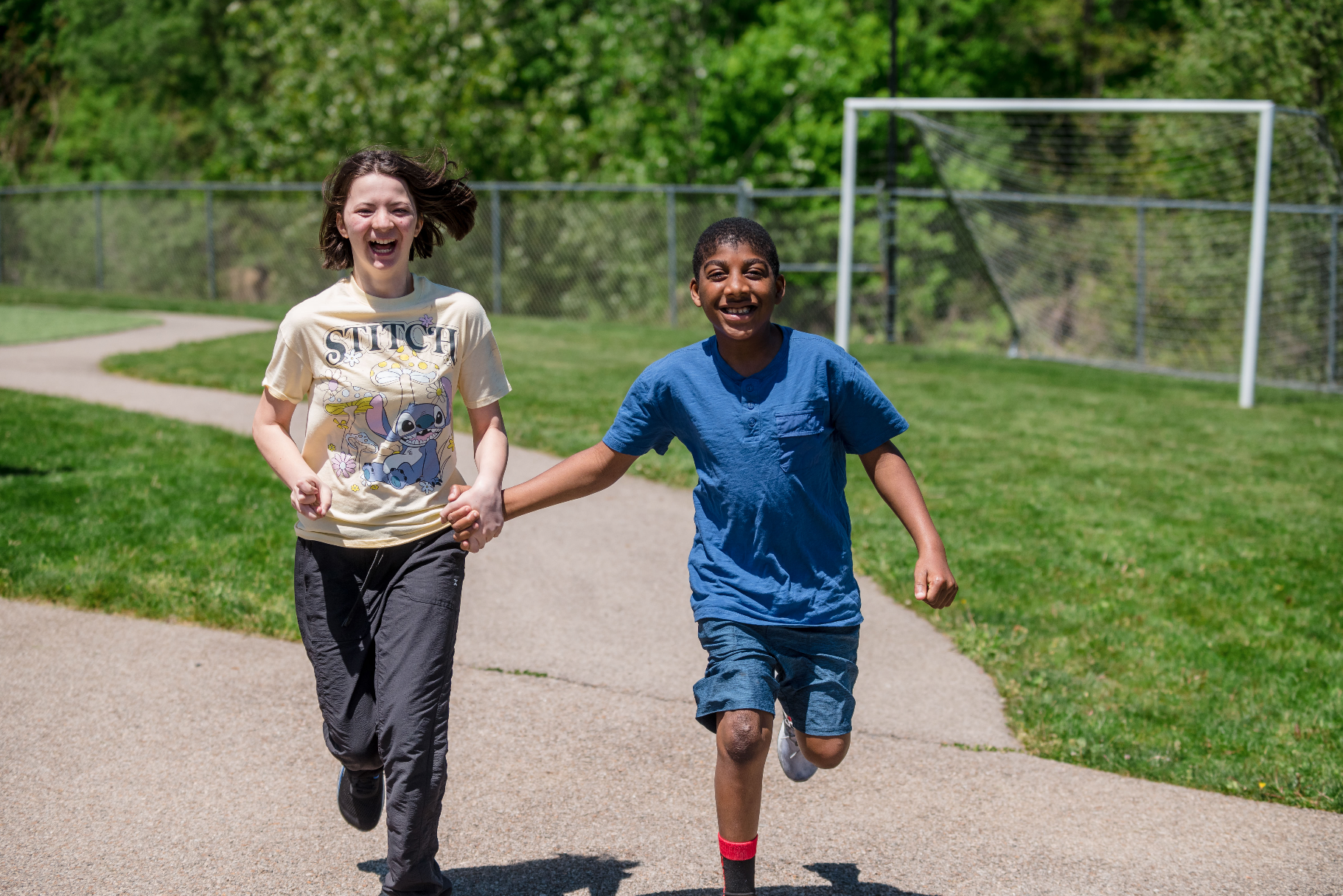 Two students holding hands and running outside.