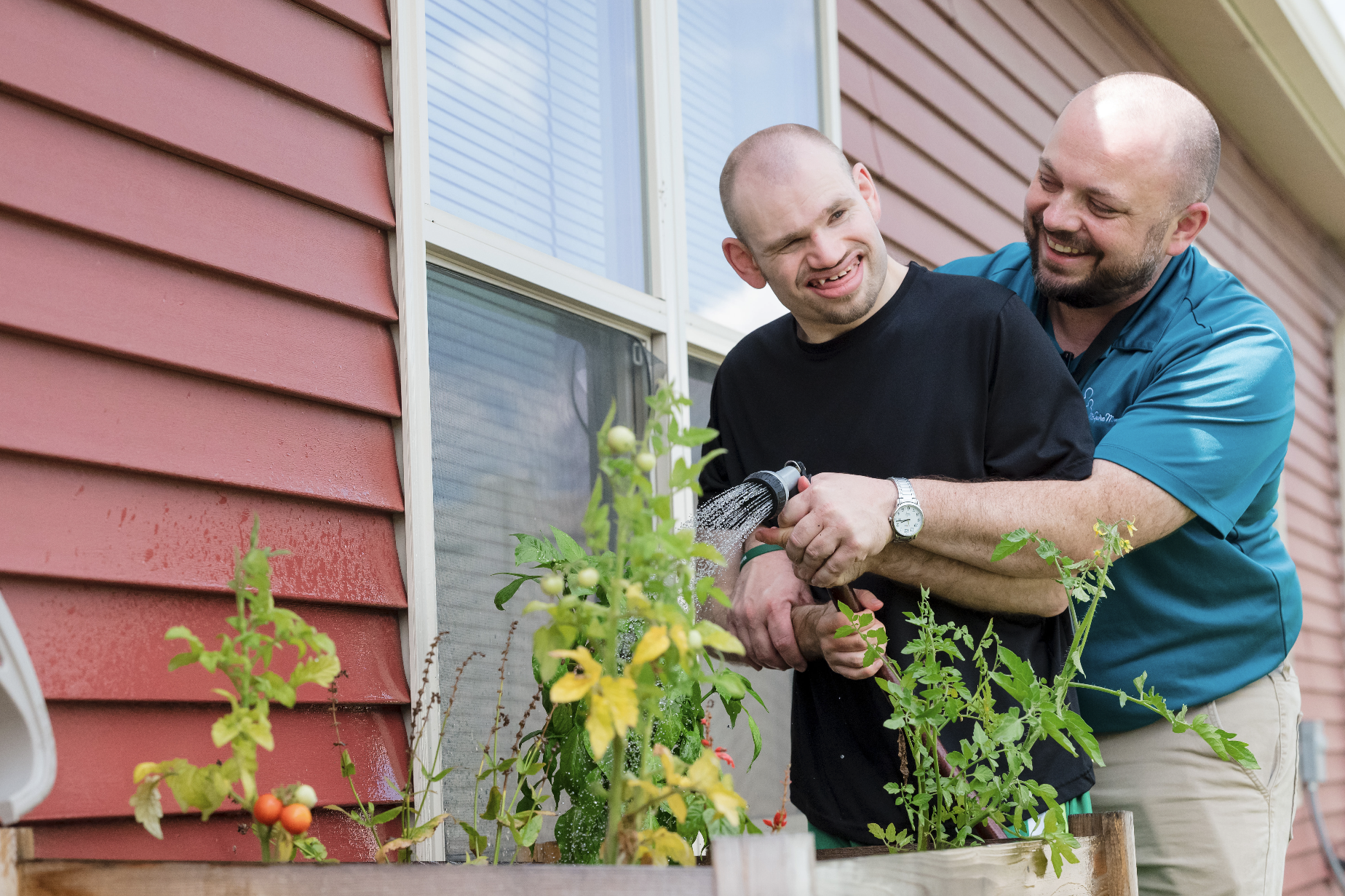 A community home resident with a McGuire Memorial team member outside a home watering plants