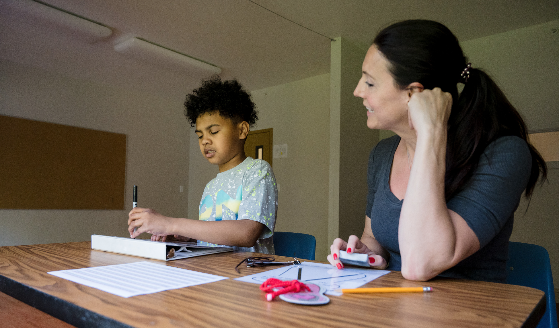 A teacher sitting next to a student as he is writing.